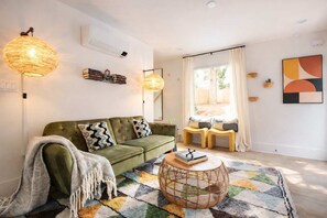 Ein gemütliches Wohnzimmer mit einem grünen Sofa, einem gemusterten Teppich und einem Korbtisch.