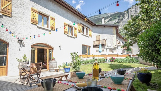 A rustic chalet with a wooden deck, outdoor dining setup, and a mountain backdrop.