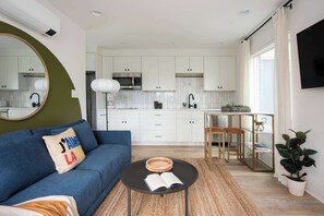 Una sala de estar moderna con un sofá azul, una mesa redonda de centro con un libro abierto y un espejo grande en la pared.
