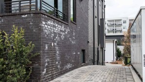 A modern building with a dark brick exterior, a paved courtyard, and a small tree. - Caviar Dreams (Atlanta)