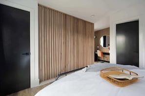 Un dormitorio moderno con una cama, un panel de pared de listones de madera, un espejo redondo y una puerta negra.