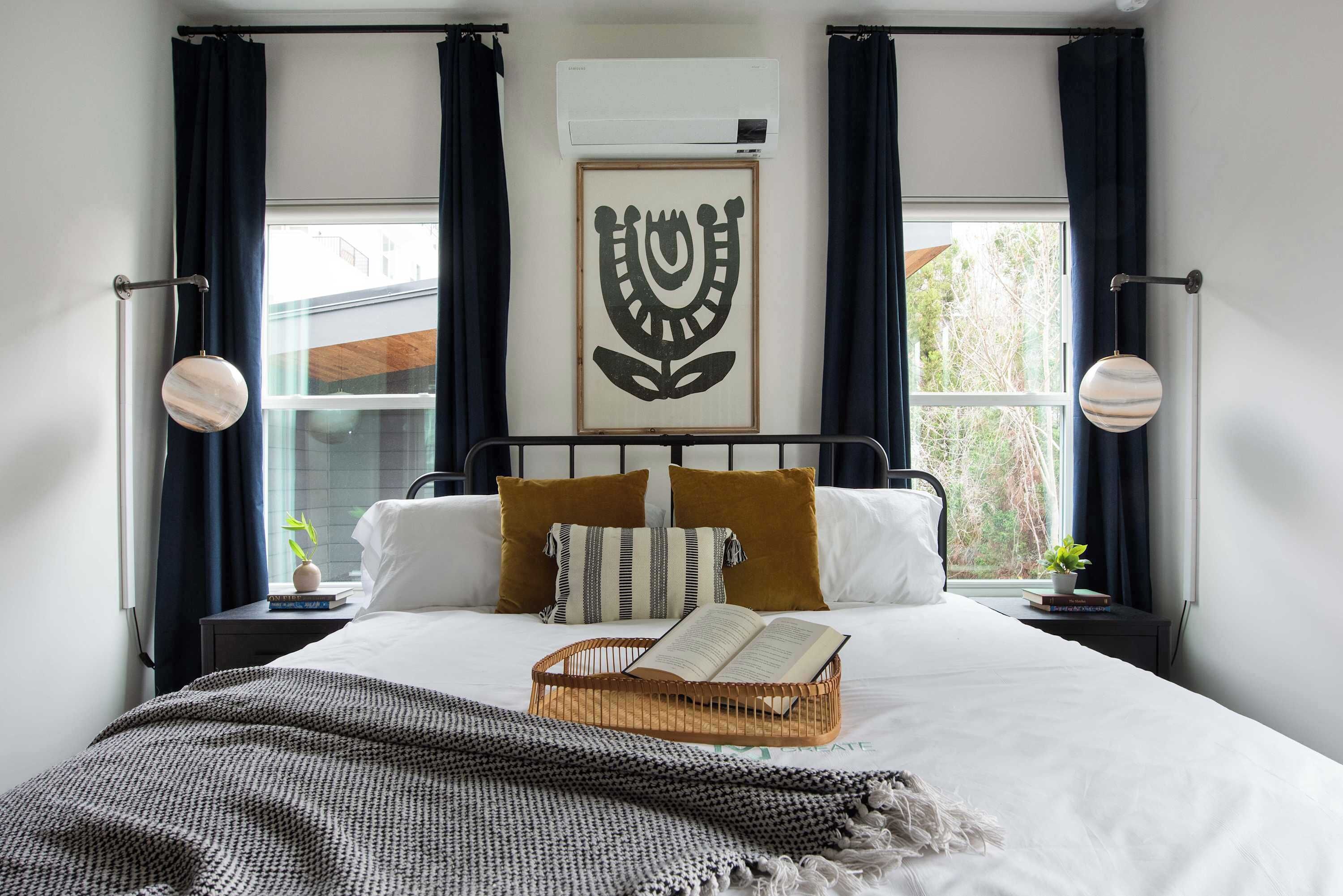 A neatly made bed with a book, a decorative wall hanging, and a window with curtains.