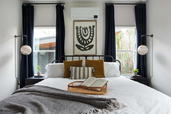 A neatly made bed with a book, a decorative wall hanging, and a window with curtains.