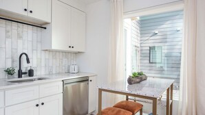 A modern kitchen with white cabinets, a stainless steel dishwasher, a marble countertop, and a small dining table with two chairs.