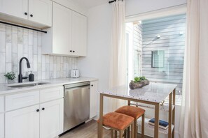 Une cuisine moderne avec des meubles blancs, un lave-vaisselle en acier inoxydable, un plan de travail en marbre et une petite table à manger avec deux chaises.