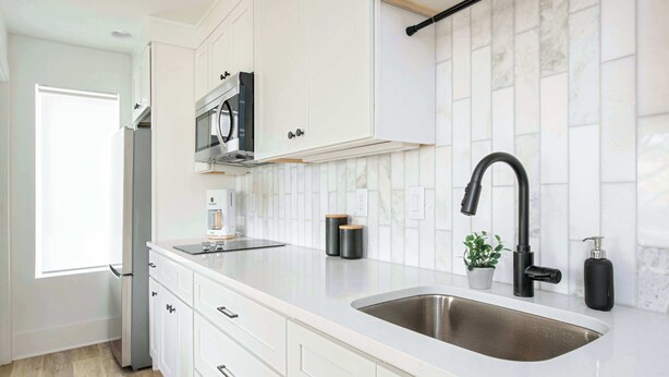 A modern kitchen with white cabinetry, a stainless steel sink, a black faucet, and a microwave. - Caviar Dreams (Atlanta)