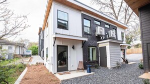 A modern two-story house with a front porch, a small garden area, and a gravel driveway.
