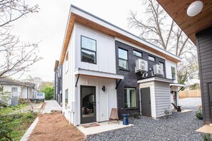 A modern two-story house with a front porch, a small garden area, and a gravel driveway.