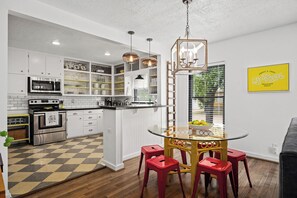A modern kitchen with white cabinetry, a central island, red stools, and a yellow sign on the wall. - Whiskey Ginger - Wine Barn, Fire Pit & More! (Fredericksburg)