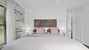 Ein Schlafzimmer mit einem großen Bett, zwei Nachttischen mit Lampen, einem Holz-Kopfteil und einer weißen Tür.