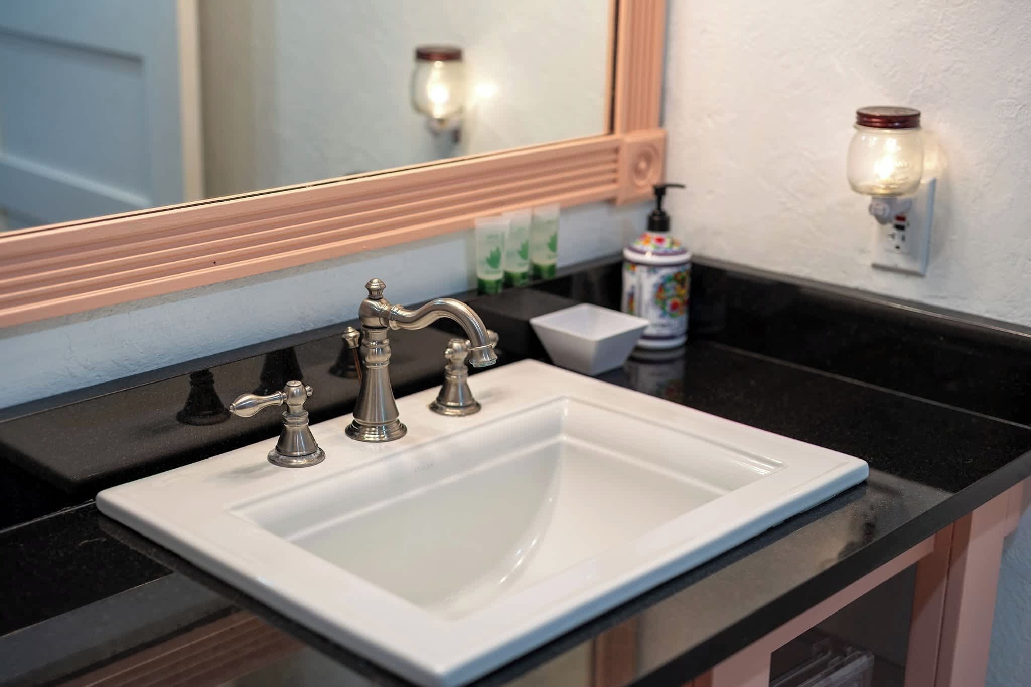 Un baño con un lavamanos blanco, un espejo con marco de madera y una lámpara de pared.