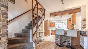 A staircase leading to a kitchen area with wooden flooring, a stone accent wall, and a bar with stools.