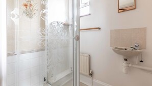 A bathroom with a glass shower enclosure, a white sink, and a radiator.