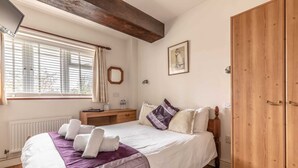 A bedroom with a bed, bedside table, wardrobe, window with curtains, and a wall-mounted picture.