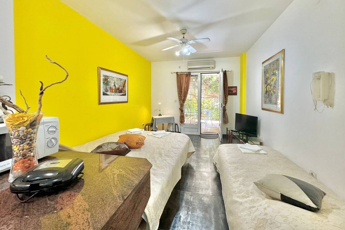 A hotel room with two beds, a desk with a computer, a ceiling fan, and a window with curtains.
