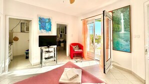 A spacious room with a ceiling fan, a television, a red chair, and a large window with a view of a waterfall. - Sun Rose apartments Sveti Stefan (Sveti Stefan)