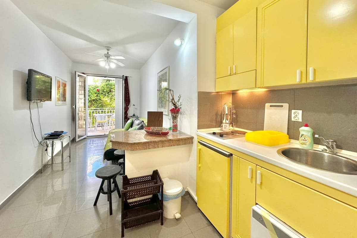 A kitchen with yellow cabinets, a sink, and a countertop. There is a dining area with a table and chairs, a ceiling fan, and a view of the outdoors.