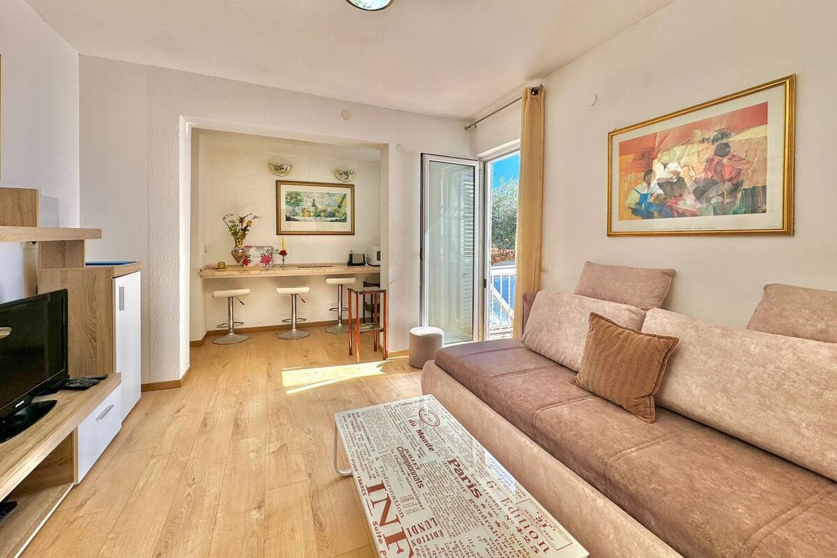 A modern living room with a sofa, a coffee table, and a TV. There is a kitchen area with a dining table and chairs.