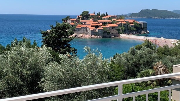 A coastal town with buildings on a rocky outcrop, a beach, and clear blue sea. - Sun Rose apartments Sveti Stefan (Sveti Stefan)