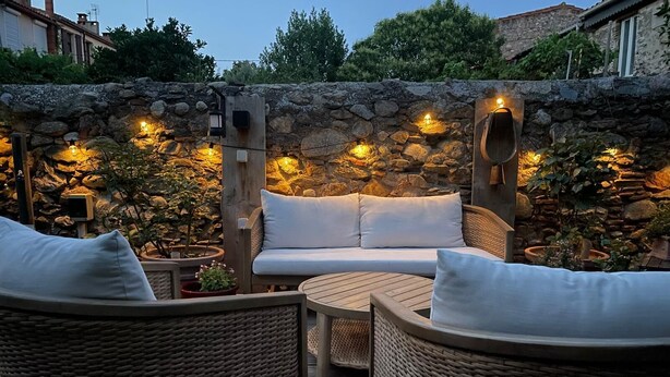 Un espacio al aire libre con mobiliario de mimbre y un muro de piedra de fondo.