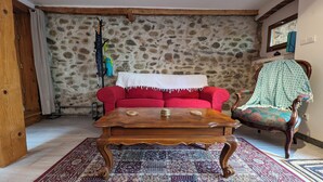 Una sala de estar acogedora con una pared de piedra, un sofá rojo, una mesa de centro de madera y una alfombra estampada.