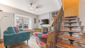 Un salón amplio con un sofá color turquesa, un sillón colorido y una escalera de madera.