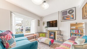 Una sala de estar acogedora con chimenea, un televisor montado en la pared y una estantería llena de libros.