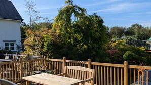 A wooden deck with a table and chairs, surrounded by a wooden railing and lush greenery. - Fell View - sleeps 4 guests  in 2 bedrooms (Portinscale)