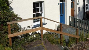 A white building with multiple windows and a blue door, surrounded by greenery and a wooden fence. - Fell View - sleeps 4 guests  in 2 bedrooms (Portinscale)