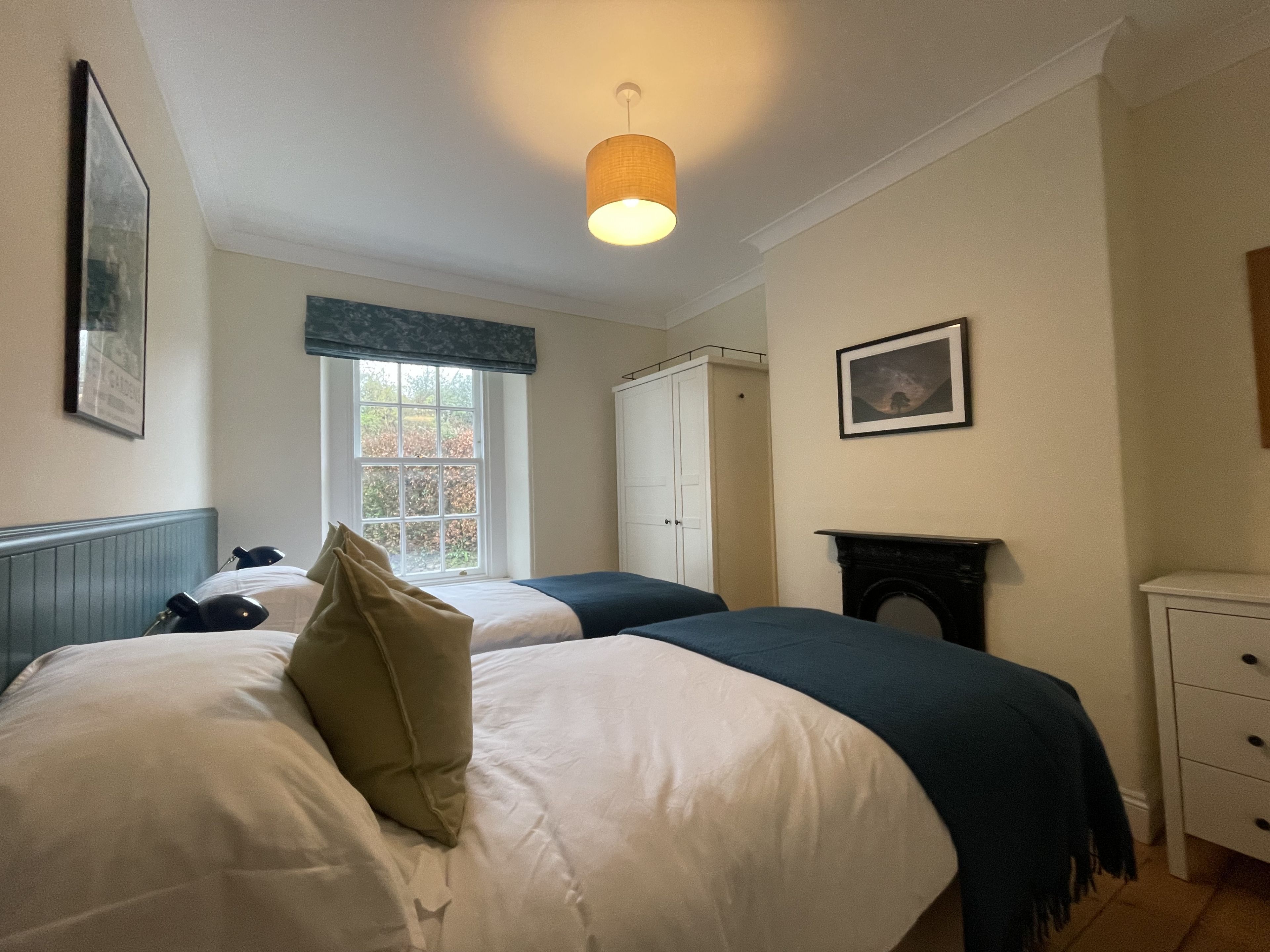 A bedroom with two beds, a window, a wardrobe, and a fireplace.