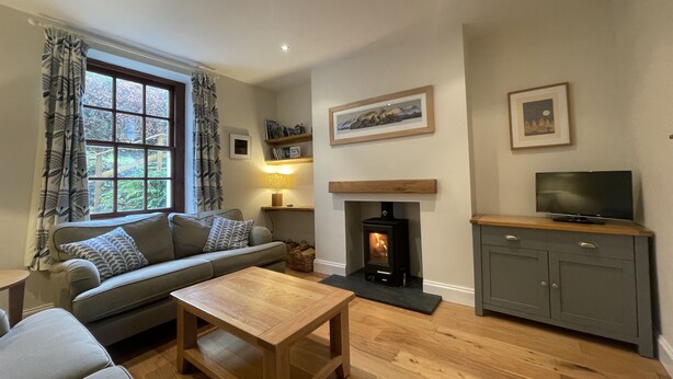 A cozy living room with a sofa, a coffee table, a fireplace, and a television on a cabinet. - Fell View - sleeps 4 guests  in 2 bedrooms (Portinscale)