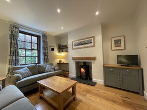 A cozy living room with a sofa, a coffee table, a fireplace, and a television on a cabinet.