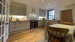 A modern kitchen with wooden cabinets, a built-in oven, a microwave, and a dining area with a table and chairs. - Fell View - sleeps 4 guests  in 2 bedrooms (Portinscale)