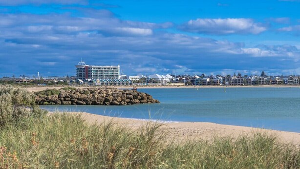 Un hôtel situé sur la côte, avec vue sur la plage, une digue rocheuse et un ciel bleu dégagé.