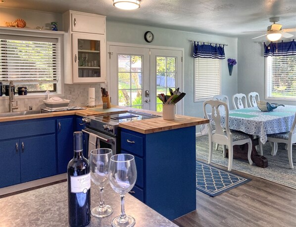 A kitchen with blue cabinets, a central island, and a dining area with white chairs and a table. - Grey Whale so close to so many beaches, hikes and more!! (Fort Bragg)