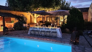 Un área de comedor al aire libre con piscina, suelo de piedra y mesas dispuestas para una comida.