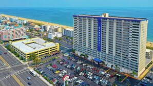 A high-rise hotel with a prominent blue sign, adjacent to a parking lot and a beach. - 2 bedroom oceanfront condo with free WiFi, 2 pools and much more in this uptown location with a great view and steps from beach! (Ocean City)