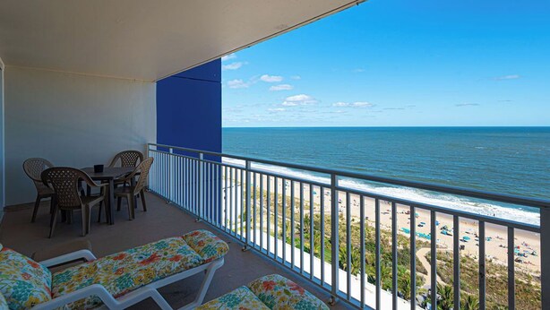 A balcony with a view of the ocean, a table with chairs, and lounge chairs. - 2 bedroom oceanfront condo with free WiFi, 2 pools and much more in this uptown location with a great view and steps from beach! (Ocean City)