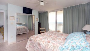A bedroom with a large bed, a ceiling fan, a TV, and a view of the ocean through a sliding door. - 2 bedroom oceanfront condo with free WiFi, 2 pools and much more in this uptown location with a great view and steps from beach! (Ocean City)
