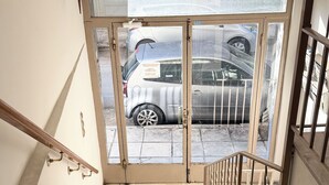 En trappa leder till en entré med en glasdörr, och utanför syns parkerade bilar.