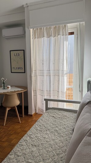 A bedroom with a bed, a bedside table with a vase of flowers, a framed picture on the wall, and a window with curtains.