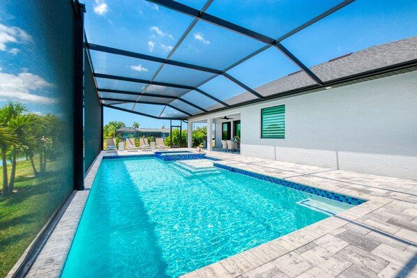A swimming pool with a glass enclosure, surrounded by a patio area with outdoor furniture.