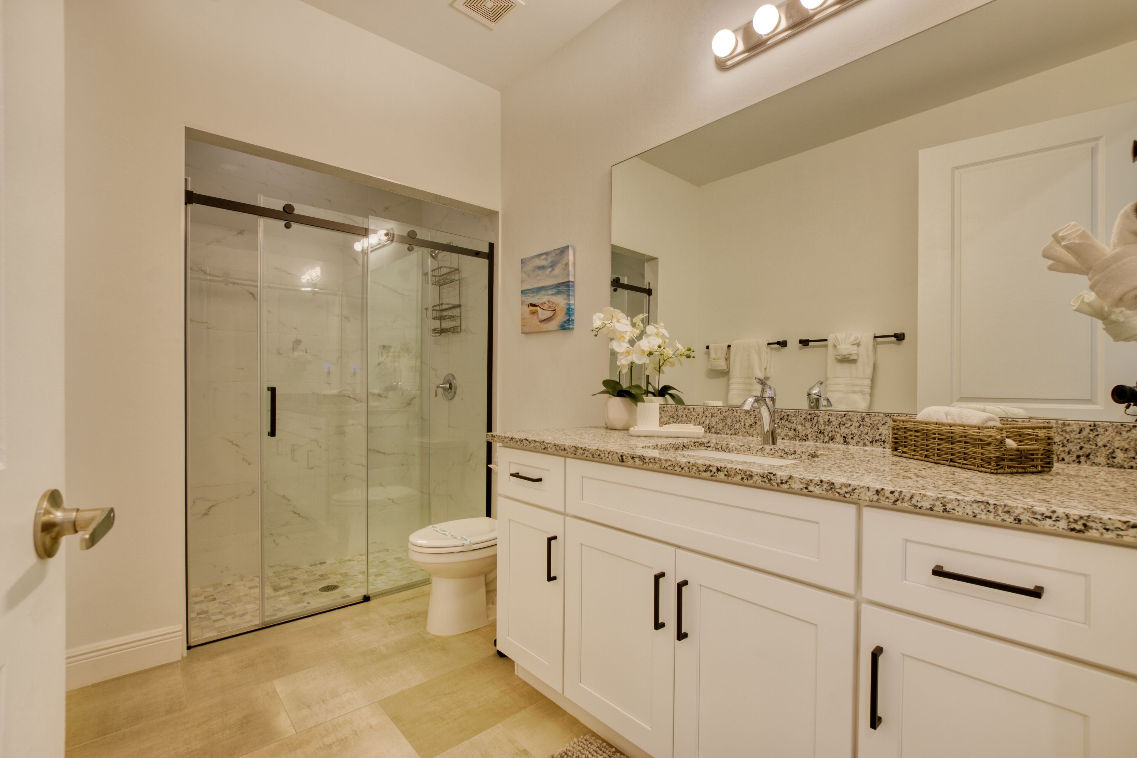 Un baño moderno con cabina de ducha de vidrio, inodoro, lavamanos con encimera de mármol y un espejo grande.