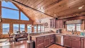 A spacious kitchen with wooden cabinets, a granite countertop, and a view of mountains through large windows. - Cabin Unwined (Morganton)