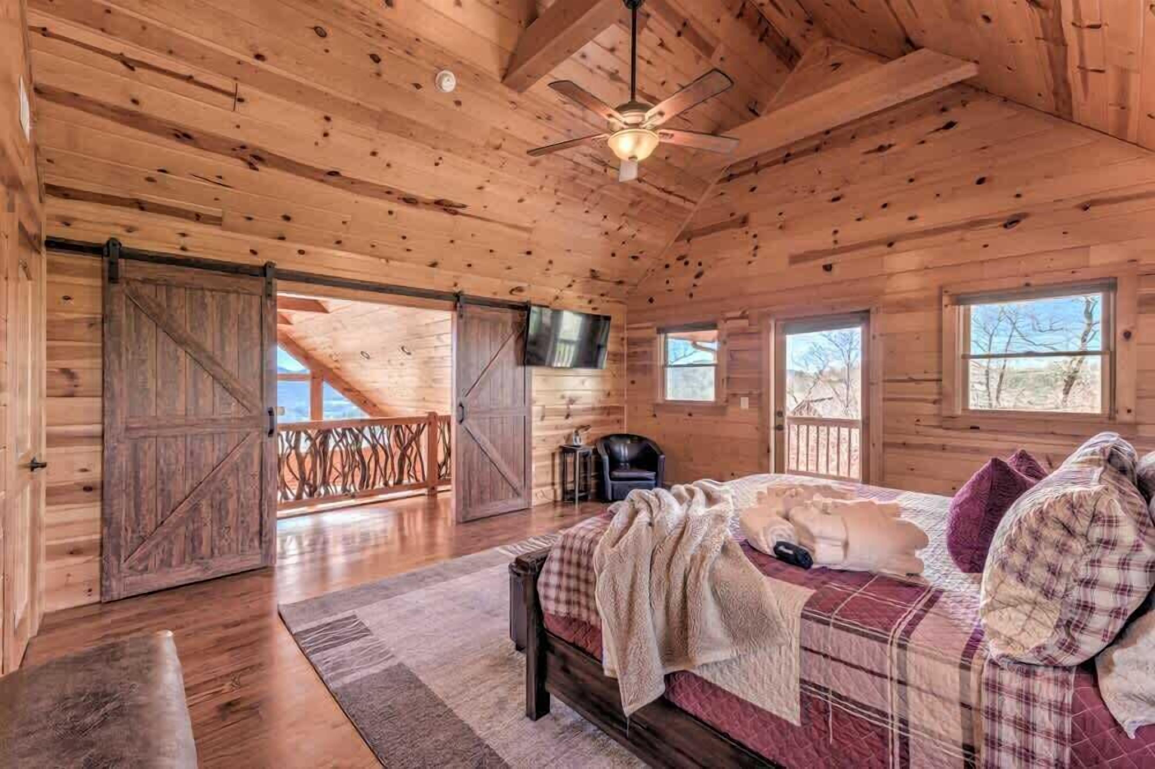 A log cabin bedroom with a bed, a ceiling fan, and a large window.
