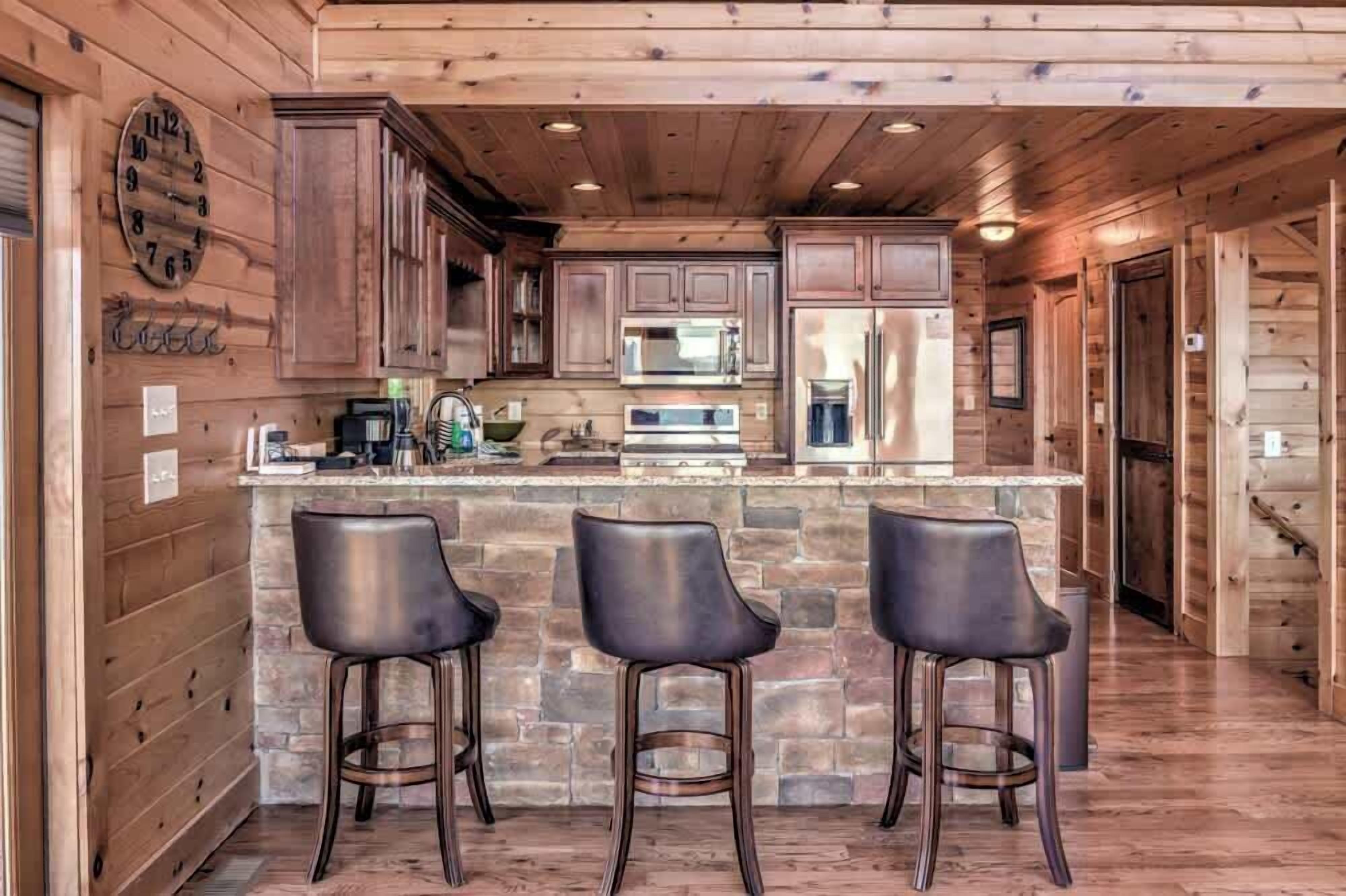 A wooden cabin interior with a kitchen featuring stone countertops, a bar area with stools, and a clock on the wall.