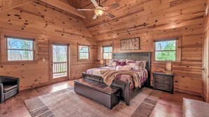 A wooden cabin bedroom with a bed, a bench, a nightstand, and a ceiling fan. - Cabin Unwined (Morganton)
