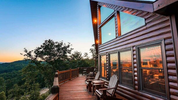 A wooden deck with outdoor seating, large windows, and a view of the surrounding landscape. - Cabin Unwined (Morganton)