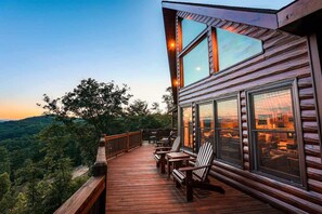 Une terrasse en bois avec des sièges d’extérieur, de grandes fenêtres et une vue sur le paysage environnant.