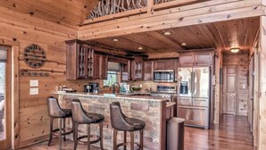 A spacious kitchen with wooden cabinets, a central island with bar stools, stainless steel appliances, and a clock on the wall. - Cabin Unwined (Morganton)